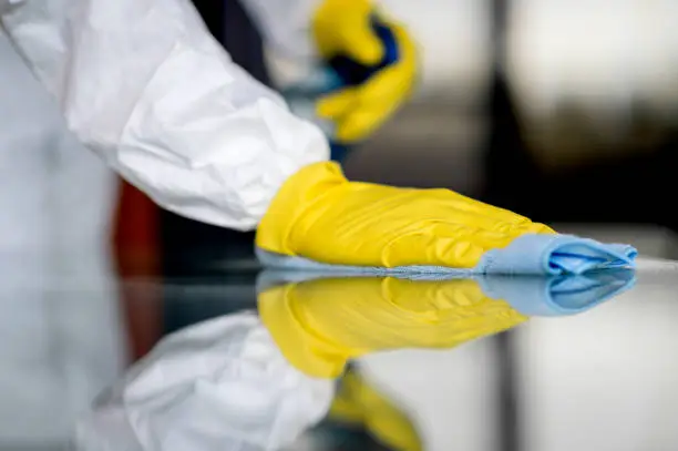 Photo of Covid-19 Wiping down surfaces. Woman with gloves and disinfectant wipe sanitizing the desk to prevent germs and bacteria infections