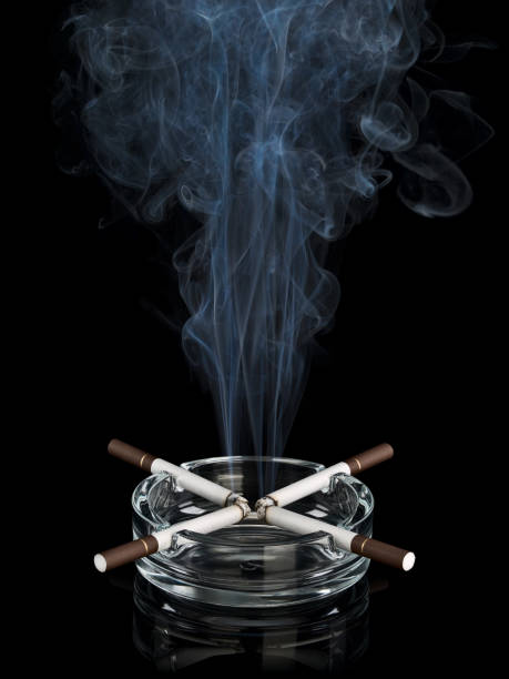 istock Curling smoke from four cigarettes in glass ashtray 1212585347