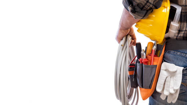 Electrician with tool belt on a white background. Electricity. View from behind, electrician holds the roll of electric cable in his hand, helmet with protective goggles. Construction industry, electrical system. Isolated on a white background. repairing electrical component stock pictures, royalty-free photos & images