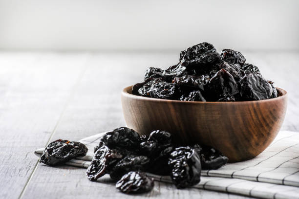 Prunes in white ceramic bowl on white rustic table. Prunes in wood bowl on white rustic table. Dried plums on white table. Fresh prunes for healthy life. prune stock pictures, royalty-free photos & images