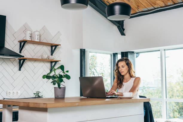 istock Woman is sitting at the kitchen table with laptop 1212597570