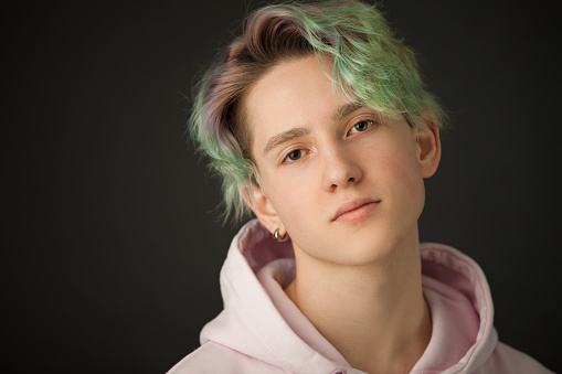 studio close-up portrait of a teenager boy with green hair in a pink hooded shirt on a black background