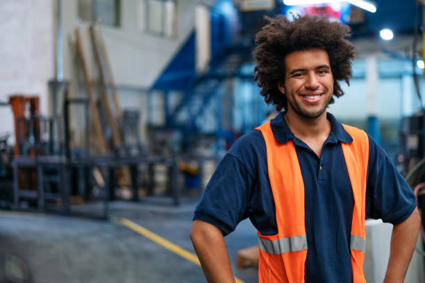 Portrait of happy young warehouse worker Portrait of a happy young man working in warehouse. Male warehouse worker in uniform looking at camera and smiling. menial job stock pictures, royalty-free photos & images