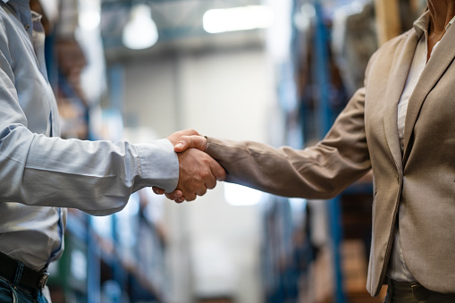 Cropped shot of female manager shaking hands with male supervisor in warehouse. Warehouse employees handshake.