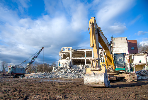 Yellow excavator with bucket at demolition of tall building. Hydraulic machine for demolish. Backhoe destroys concrete of the old structures on construction site