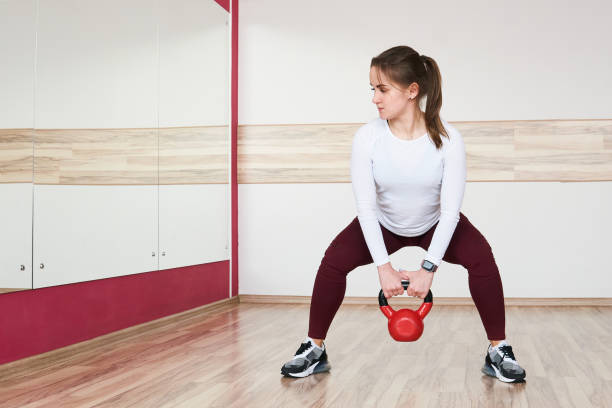 jovem mulher está treinando com kettlebell na academia olhando no espelho - kettle bell sport women muscular build - fotografias e filmes do acervo