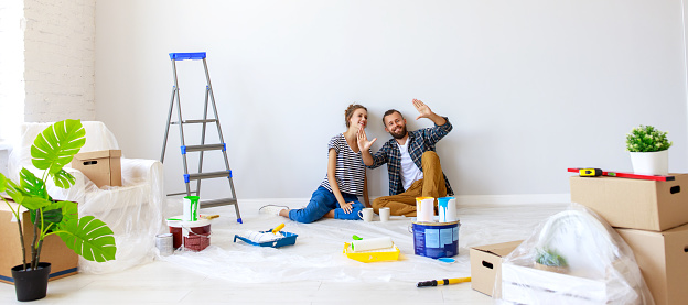 Young couple woman and boyfriend pointing away  while sitting near white wall and planning room interior during renovation in new apartment