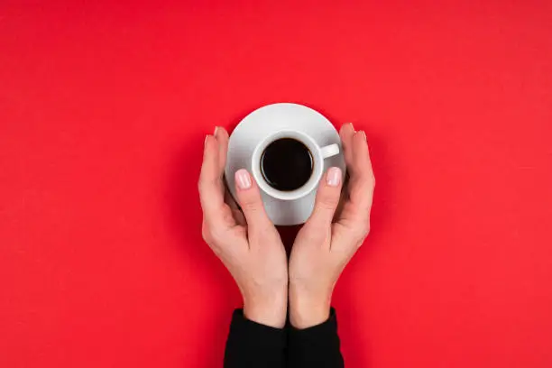 Photo of Hands holds a cup of coffee isolated on red background