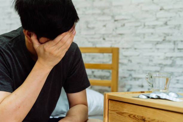 istock Young Asian man feeling sick and taking pills while sitting on the bed at home 1212623080