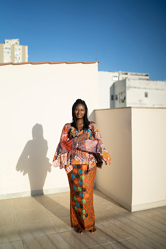 African woman in traditional dress standing on terrace. Woman in official dress standing on balcony in hotel.