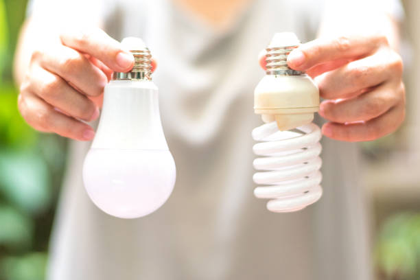 concept d’économie d’énergie. l’homme d’asie changeant des ampoules compact-fluorescentes (cfl) avec la nouvelle ampoule led. - compact fluorescent lightbulb photos photos et images de collection