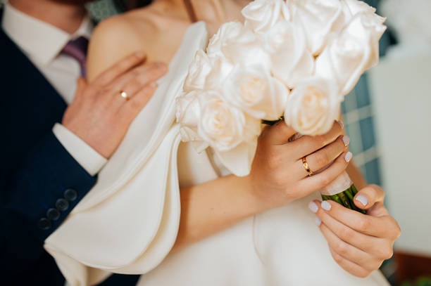 foto de boda con estilo. la novia en un vestido blanco elegante hecho de tela rígida con una exuberante manga con volantes en un vestido de novia inusual con un volante blanco de rosas en los brazos de los hombres. - puffed sleeve fotografías e imágenes de stock