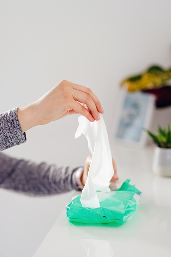 Close up on woman's hands unknown female hand taking wet napkin towel tissue from the box container package on the white shelf at home or office antibacterial disinfection alcohol hygiene product