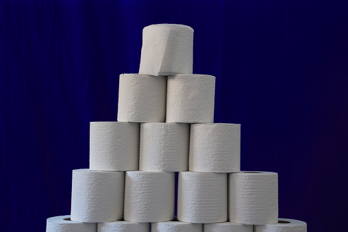 Toilet paper roll stacked in an organized pyramid against a blue background.