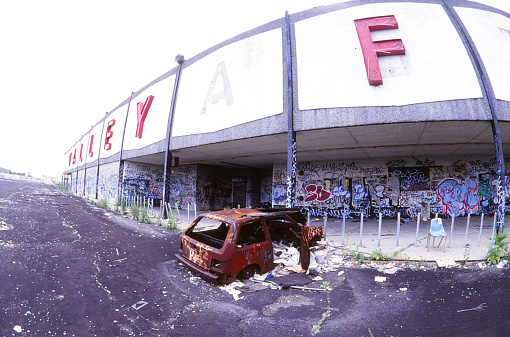 A burned-out car in front of an abandoned mall shot with a rectilinear fish-eye lens.
