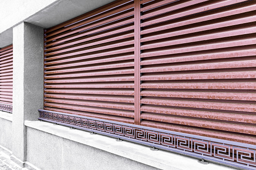 facade of modern building with windows row, red metal protective blinds and wrought metal railings
