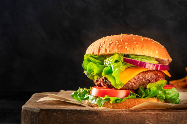 istock Burger with beef, cheese, onion, tomato, and green salad, a side view on a dark background with copy space 1212657612