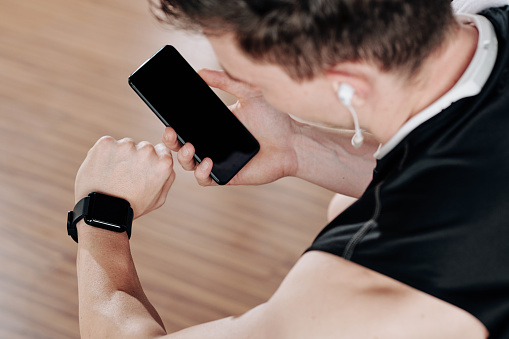 Sportsman synchronizing smartphone with smart watch on his wrist before training in gym