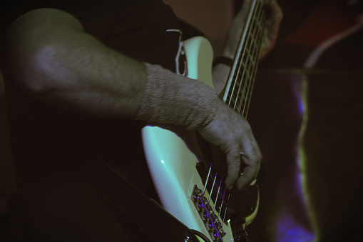 A man plays bass guitar on stage. Hand close-up. Soft focus, Motion blur