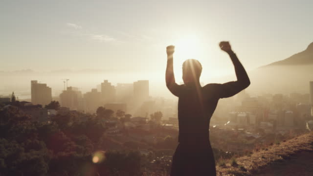 4k video footage of a young man celebrating an accomplishment while jogging on a mountain against an urban background