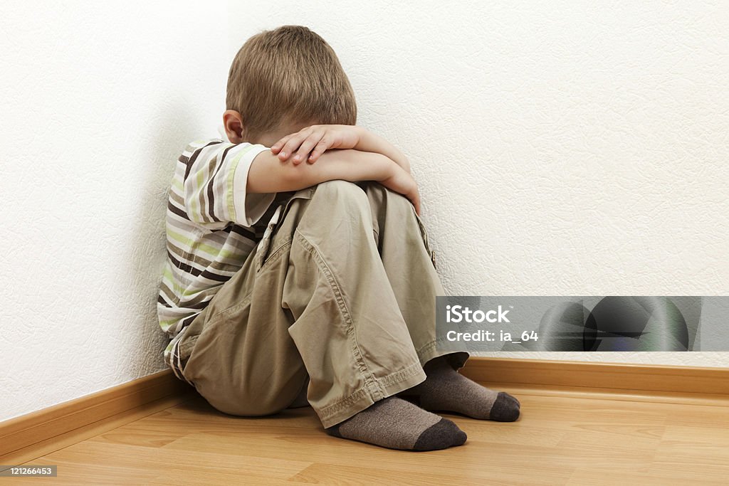 Young boy sitting in corner with head bowed into chest Little child boy wall corner punishment sitting Boys Stock Photo