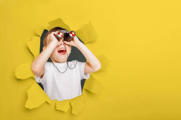 istock Happy cute boy is having looking through binoculars on the yellow paper backgrounds 1212666861