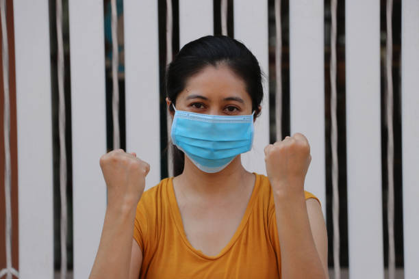가면을 쓴 아시아 여성이 세균을 예방합니다. 작은 입자 또는 바이러스 코로나 또는 covid 19 보호. 비행을 의미하기 위해 주먹을 들어 올립니다. - taint 뉴스 사진 이미지
