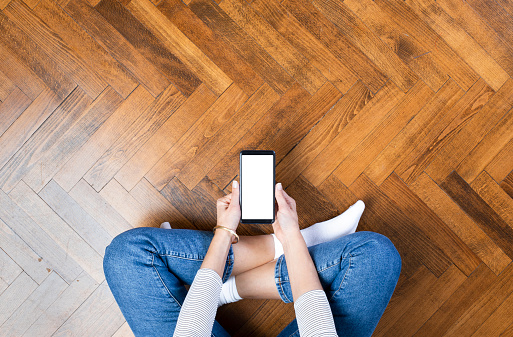 Young woman sitting on the floor at home and using a mobile phone. Directly above
