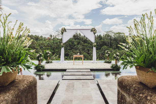 White Wedding ceremony arch in tropical jungle on edge of blue infinity swimming pool. White Wedding ceremony arch in tropical jungle on edge of blue infinity swimming pool. Beautiful arch and decorations on the cliff. table ledge stock pictures, royalty-free photos & images