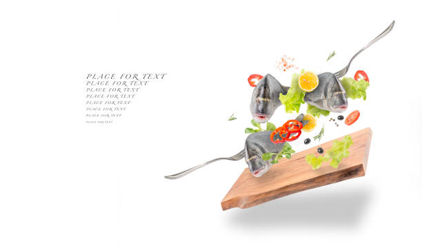 Fish with vegetables on a white background with spices and herbs falling into a pan with a lid on a wooden oak Board.