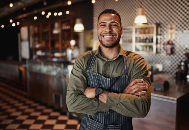 istock Afro-american cafe owner standing smiling wearing apron with folded arms 1212669748