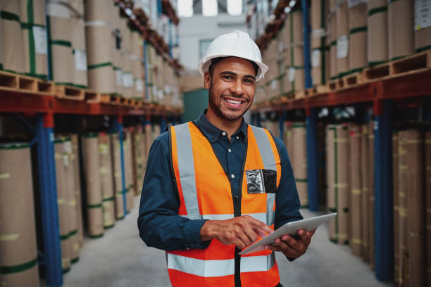 felice manager di fabbrica maschio che usa tablet digitale in magazzino mentre si trova contro lo scaffale delle merci guardando la fotocamera - warehouse freight transportation checklist industry foto e immagini stock