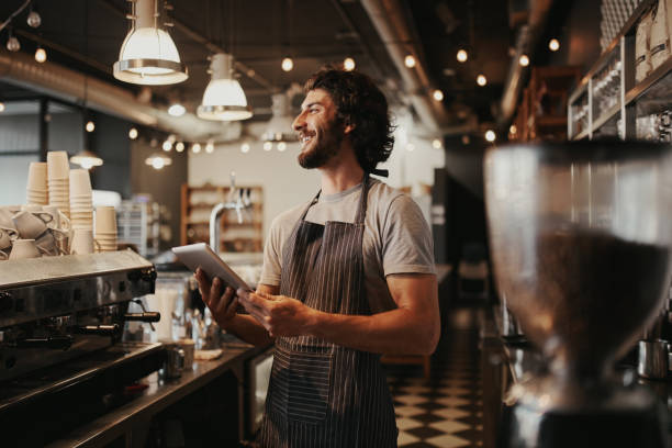 istock Handsome caucasian man in coffee shop laughing while holding digital tablet in hand standing behind counter 1212669800
