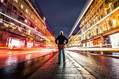 One man on busy city street at night long exposure with blurred motion
