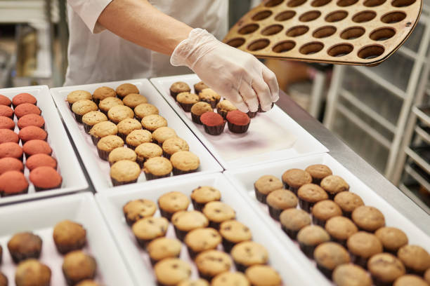 istock Male Chef Placing Baked Cupcakes onto Tray for Icing 1212674668