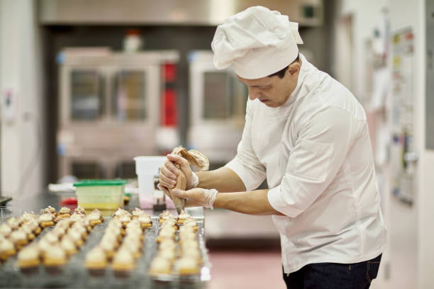 istock Hispanic American Male Chef Icing Cupcakes in Vegan Bakery 1212674752