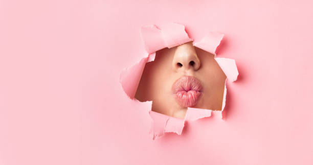 Unrecognizable Girl Pouting Lips Through Hole In Paper, Beauty Background Unrecognizable Girl Pouting Lips Through Hole In Pink Paper. Makeup, Beauty Background. Panorama, Copy Space puckering stock pictures, royalty-free photos & images