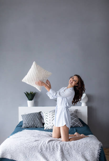 istock Joyful woman on the bed throwing cushions. 1212677125