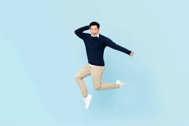 Smiling young handsome Asian man jumping on light blue studio background