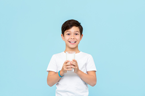 Happy smiling Mixed race boy drinking fresh milk isolated on light blue studio background