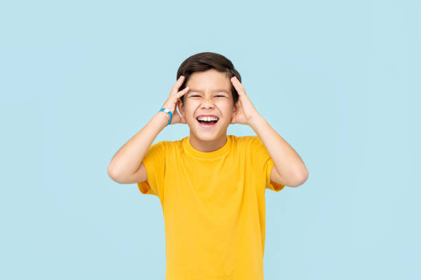 feliz menino asiático sorridente com as mãos apertando a cabeça isolada em fundo azul claro - child excitement awe fun - fotografias e filmes do acervo