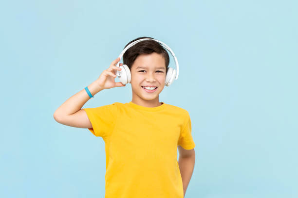 felice ragazzo sorridente di razza mista che indossa cuffie wireless ascoltando musica isolata su sfondo azzurro - music listening child smiling foto e immagini stock