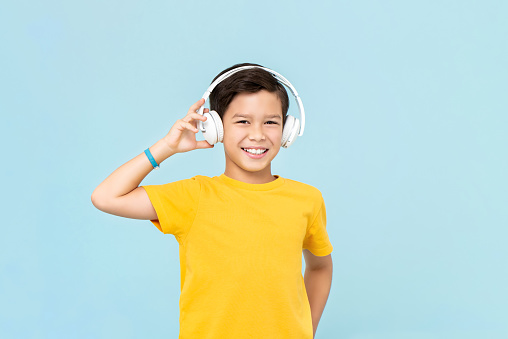 Happy smiling mixed-race boy wearing wireless headphones listening to music isolated on light blue background