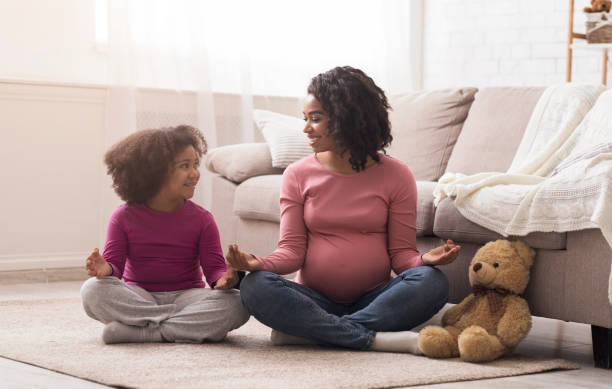 pregnant black mother and her little daughter practicing youga at home - relaxation exercise child mother human pregnancy imagens e fotografias de stock