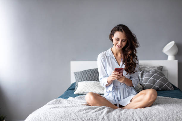 istock Smiling woman with phone on the bed. Use mobile internet. 1212678063