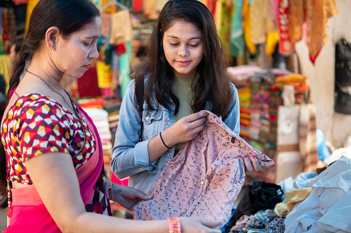 Happy mother and daughter looking and buying clothes together from outdoor street market of Delhi, India at day time.