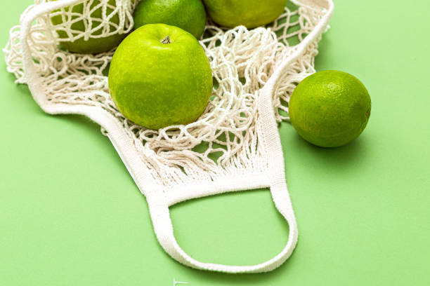 istock Net bag with green fruits on a green background. Zero waste. Monochrome 1212680784