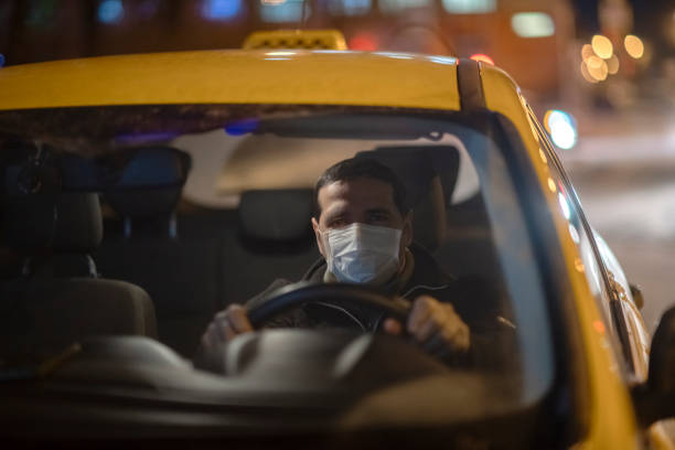 taxi driver wearing protective medical mask on a city street at night - illness mask pollution car imagens e fotografias de stock