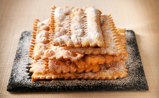 Speciality Italian chiacchiere, sweet carnival cookies of deep fried crispy dough sprinkled with powdered sugar stacked on a tray in close up
