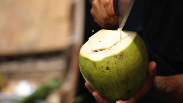 Close up of man cutting a coconut with knife ,at the floating market in Thailand.